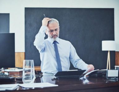 Chef d'entreprise Homme d'affaires en chemise, pensif, devant un bureau avec un téléphone et un verre d'eau.